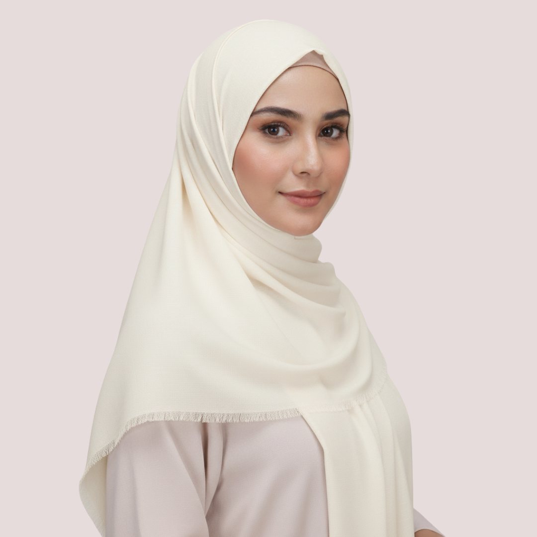 Woman wearing a light-colored hijab against a plain background